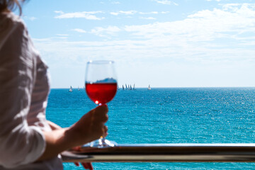Defocused beautiful woman standing on a balcony of apartments with rose wine glass in your hand and looking at the sea.