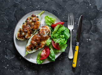 Chicken, spinach, mushrooms, mozzarella cheese stuffed roasted zucchini and fresh vegetable salad on a dark background, top view