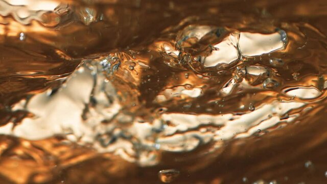Boiling liquid gold with ice cubes. Elegant slow-motion footage of a high-end drink in extreme close-up