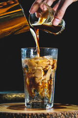 Iced coffee mixed with milk together served in a glass on wood and black background 