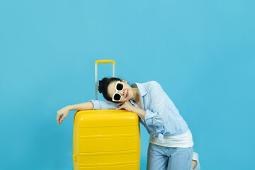 Summer holidays, vacation and travel concept.Happy traveler tourist beautiful young asian woman in casual clothes and sunglasses with yellow suitcase or luggage bag isolated on blue background