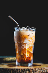 Cold fresh thai ice tea coffee served with coconut milk and metal straw with ice cubes on wood table and black background 