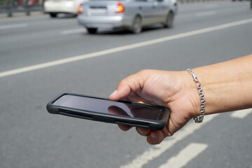  Mobile phone in a female hand on the background of the highway with cars.