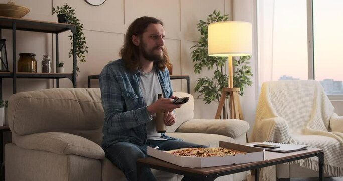 Man eating pizza and drinking beer while watching tv at home
