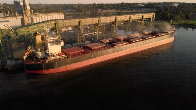 Aerial drone footage of a industrial grain elevator and a cargo ship being loaded in the port of Vancouver at sunset. 4K 24FPS.