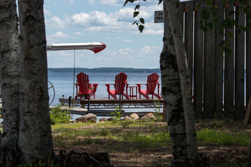 Obraz na płótnie Canvas Three red muskoka chairs on a dock looking out into the lake 
