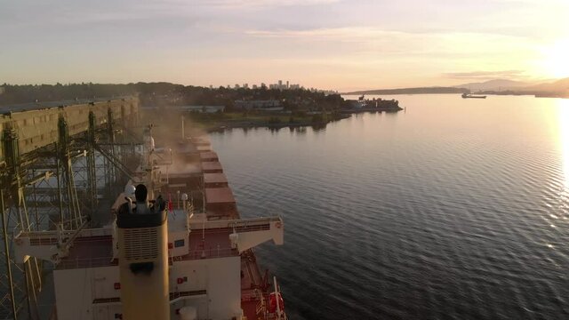Aerial drone footage of a industrial grain elevator and a cargo ship being loaded in the port of Vancouver at sunset. 4K 24FPS.