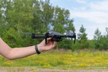 Black drone in the hand of a child. Background - green forest, yellow meadow, blue sky. Concept - drone launch summer.