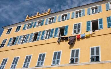 Fototapeta na wymiar Traditional colorful painted building facade with blue shutters and laundry hanging in Bastia, Corsica, France