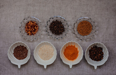 Spices and grains in clear glass and in white cups on a napkin. Top view