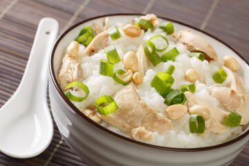 Chinese cooking, congee jook boiling rice with a lot of water over low heat with the addition of chicken, peanuts and green onions close-up in a bowl. Horizontal