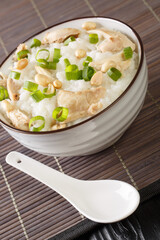 Rice porridge with boiled chicken, peanuts and green onions close-up in a bowl on the table. vertical