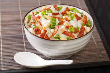 Asian rice porridge with bacon, peanuts and green onions close-up in a bowl on the table. horizontal