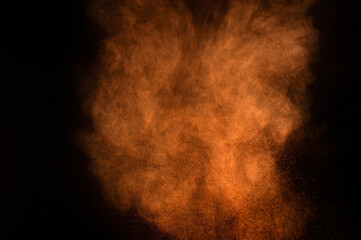 Orange powder explosion on black background. Colored powder cloud. Colorful dust explode. Paint Holi.