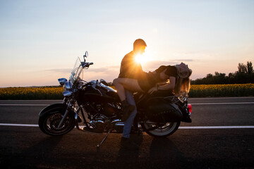 Fototapeta na wymiar Bikers man and woman stopped at the side of the road to rest and kiss passionately. Photos of loving motorcyclists at sunset. The concept of freedom, brutality and passion