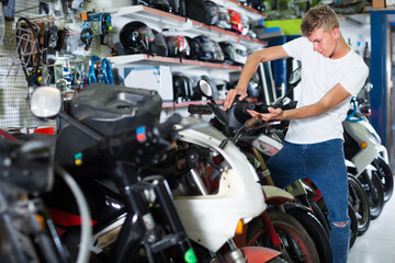 Fototapeta na wymiar Young calm man motorcyclist choosing the bike from assortment in the shop.