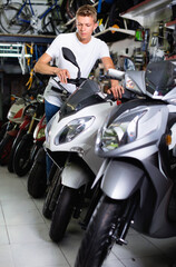 Fototapeta na wymiar Portrait of adult cheerful positive man purchaser choosing motorbike in the store