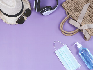 COVID-19 prevention , travel and new normal concept, top view of   woven bag with  surgical mask and sanitizer gel and women's vacation  accessories on purple  background.