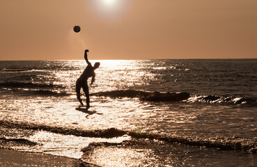 Silhouette of a boy playing goaltender in the ocean that throws a ball to his friend on the beach during  summer vacation.