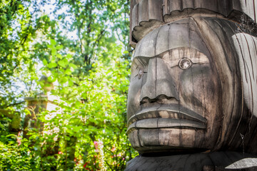 Partial large wood carving of woman face, outdoors. Indigenous carving art. Soft blurred tree background. North Vancouver, British Columbia, Canada