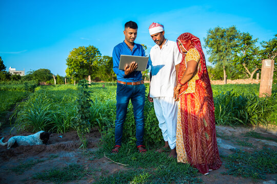 Young Indian Man With Laptop Showing Something To Village Farmer Family On Internet Standing In Green Field, Agriculture Land, Teaching Computer And Use Of Technology.