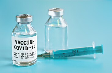Glass vial with label Covid 19 vaccine (own design, not real product), another bottle and hypodermic syringe needle near, light blue background