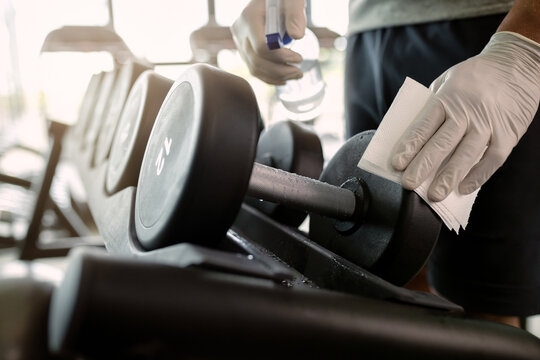 Close-up of athlete disinfecting hand weights in a gym.