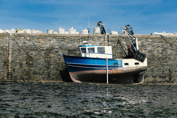 A blue fishing boat is on dry ground in the harbor at low tide