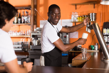 Fototapeta premium Young man barman is pouring unbottled beer for client in bar..