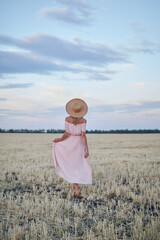 Young woman in hat and pink dress on the field by sunset light