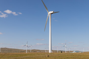 Fototapeta premium wind turbine, or wind energy converter, converts the wind's kinetic energy into electrical energy in Huanghuagou Huitengxile near Hohhot, Inner Mongolia, China, with horse, clouds and blue sky