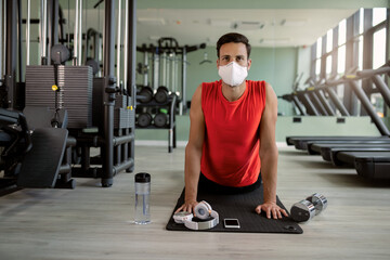 Athletic man with protective face mask doing stretching exercises in a gym