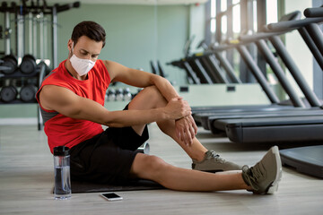 Fototapeta na wymiar Young athletic man with face mask taking a break while having sports training in a gym
