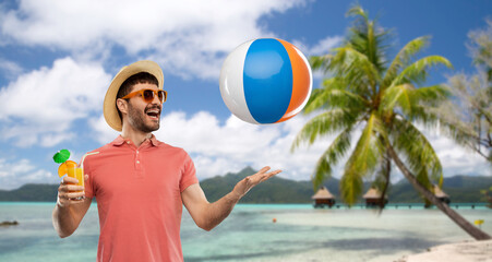 summer, vacation and people concept - happy smiling young man in sunglasses and straw hat with orange juice cocktail and inflatable beach ball over tropical beach background in french polynesia