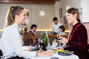 Friendly meeting of two young women over dinner with wine in restaurant. Focus on right woman