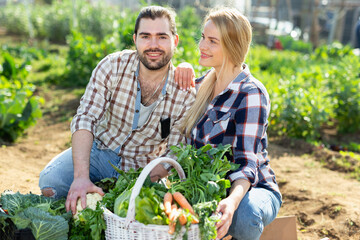 Obraz premium Cheerful couple of farmers holding baskets of harvest at garden