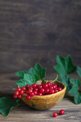 Red currant with leaves in bowl on rustic wooden table