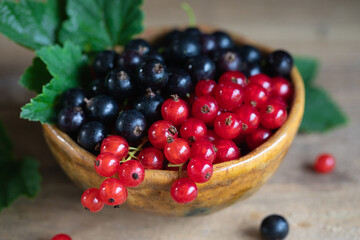 Red and black currant, gooseberry in ceramic bowl on a wooden background