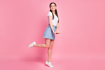 Full length profile photo of pretty cheerful lady street look outfit flirty mood wear casual white t-shirt mini denim skirt sneakers isolated pastel pink color background