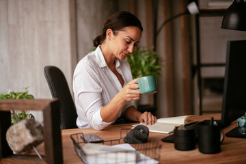 Young businesswoman drinking coffee in her office. Beautiful businesswoman enjoying in the mornings.	
