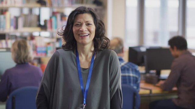 Portrait of smiling mature female teacher or student in library with other students studying in background - shot in slow motion