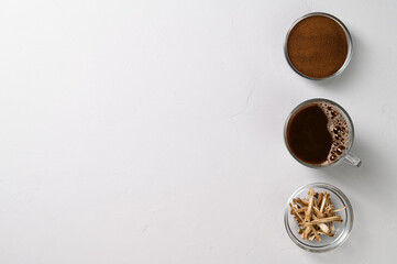 A healthy drink, an alternative to coffee. Chicory drink in a glass cup, dried roots and powder in bowls on a light gray stone background. Top view, space for text.