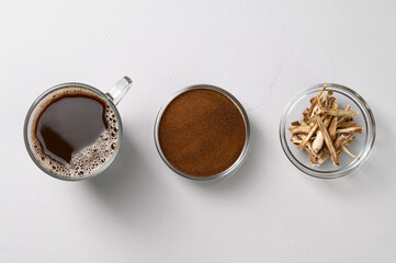 A healthy drink, an alternative to coffee. Chicory drink in a glass cup, dried roots and powder in bowls on a light gray stone background. Top view, space for text.