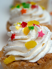 Several cakes in a row close-up. The whipped cream lies in a spiral on a shortcrust pastry basket. The top of the cream is sprinkled with decorative pastry decorations.