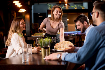 Waiter woman serving group of friends with food in the restaurant