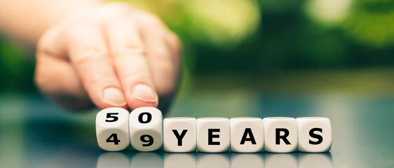 Hand turns dice and changes the expression "49 years" to "50 years".