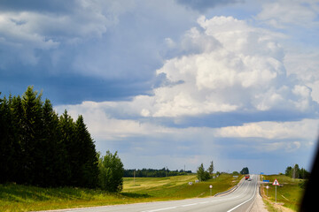 Beautiful landscape with blue sky, white clouds and the road that goes to the horizon with the forest and trees on the roadsides