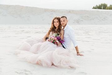 Love Story of a beautiful couple in a pink wedding luxury dress with a bouquet in the Sahara desert, sand, dunes