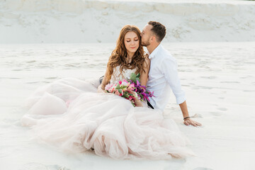 Love Story of a beautiful couple in a pink wedding luxury dress with a bouquet in the Sahara desert, sand, dunes