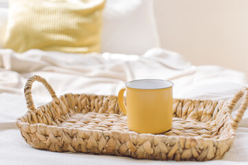 Fototapeta na wymiar Yellow mockup cup on wicker tray on bed.